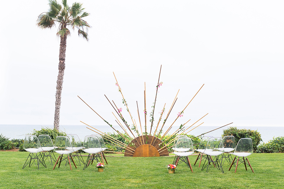 Ole-Hanson-Beach-Club-ceremony-space-with-a-geometric-sun-like-décor-where-the-ceremony-would-take-place-and-white-and-wood-chairs-on-a-green-lawn