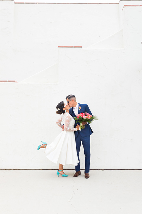 Ole-Hanson-Beach-Club-groom-kissing-bride-bride-kciking-her-heel-up-the-bride-wore-a-tea-length-gown-with-lace-sleeves-and-teal-retro-inspired-heels-the-groom-wore-a-dark-blue-suit-with-a-light-pink-long-tie-and-brown-shoes
