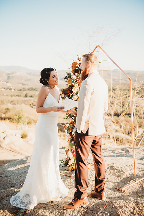 Moonflower-Ranch-Shoot-bride-and-groom-at-ceremony-bride-in-a-lace-form-fitting-gown-with-straps-and-v-neck-line-groom-in-a-tan-suit-jacket-with-burgundy-pants-and-floral-necktie