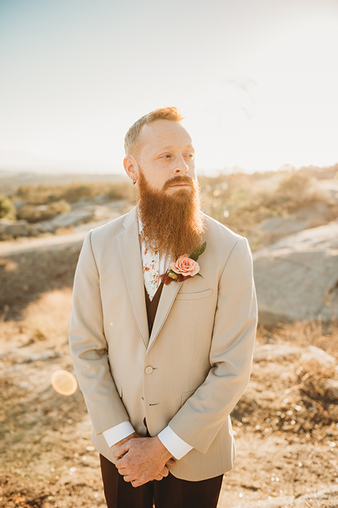 Moonflower-Ranch-Shoot-groom-crossing-hands-close-up-in-a-tan-suit-jacket-with-burgundy-pants-and-floral-necktie