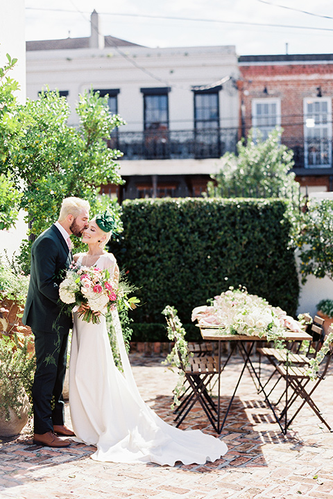 II-Mercato-in-New-Orleans-bride-and-groom-standing-next-to-table-bride-in-a-fitting-minimalistic-dress-with-a-high-neckline-and-floral-crown-groom-in-a-green-suit-with-brown-shoes-and-floral-long-tie