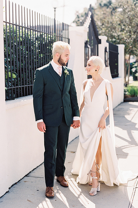 II-Mercato-in-New-Orleans-bride-and-groom-walking-outside-bride-in-a-fitting-minimalistic-dress-with-a-high-neckline-and-floral-crown-groom-in-a-green-suit-with-brown-shoes-and-floral-long-tie