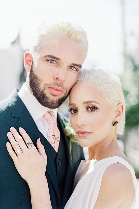 II-Mercato-in-New-Orleans-close-up-on-bride-and-groom-bride-in-a-fitting-minimalistic-dress-with-a-high-neckline-and-floral-crown-groom-in-a-green-suit-with-brown-shoes-and-floral-long-tie