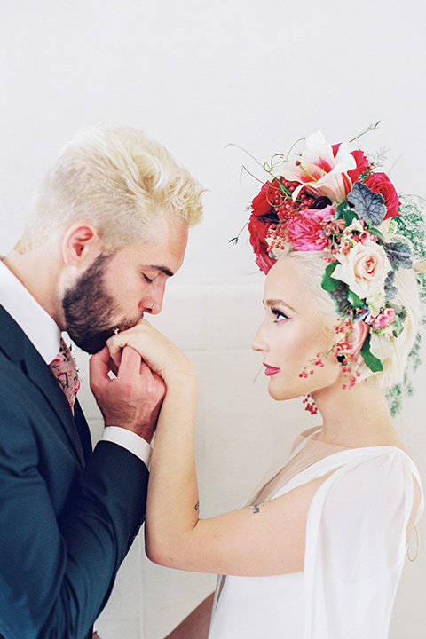 II-Mercato-in-New-Orleans-groom-kissing-brides-hand-bride-in-a-fitting-minimalistic-dress-with-a-high-neckline-and-floral-crown-groom-in-a-green-suit-with-brown-shoes-and-floral-long-tie