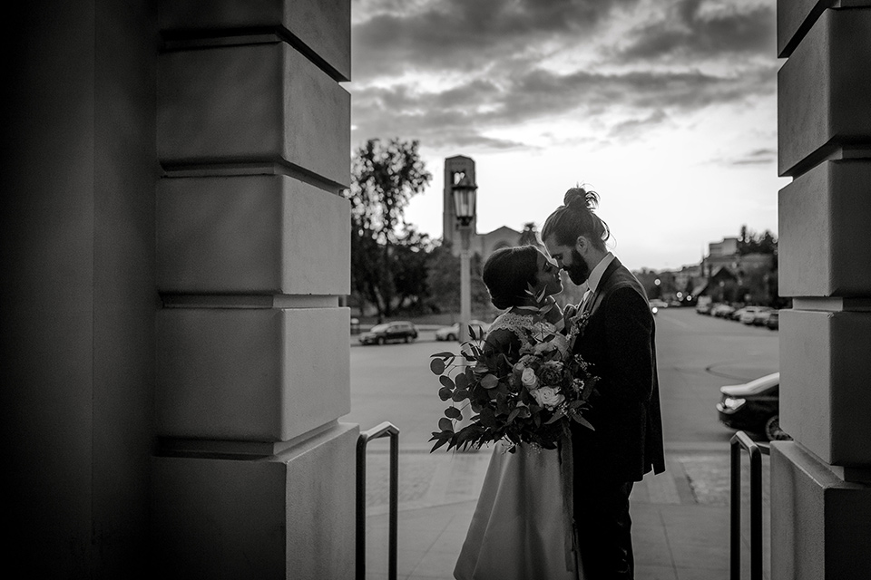 Pasadena-city-hall-styled-shoot-black-and-white-photo-of-couple-touching-heads-bride-in-a-short-dress-with-cap-sleeves-groom-in-a-navy-shawl-lapel-tuxedo