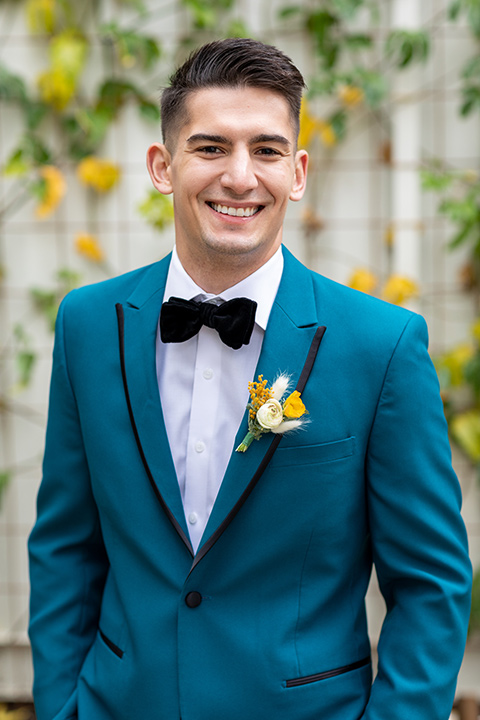 the groom in a teal tuxedo coat with black pants and a black bow tie 