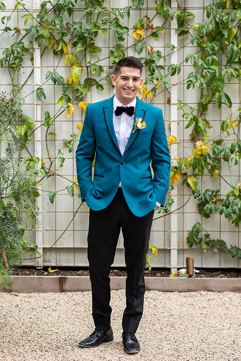 the groom in a teal tuxedo coat with black pants and a black bow tie