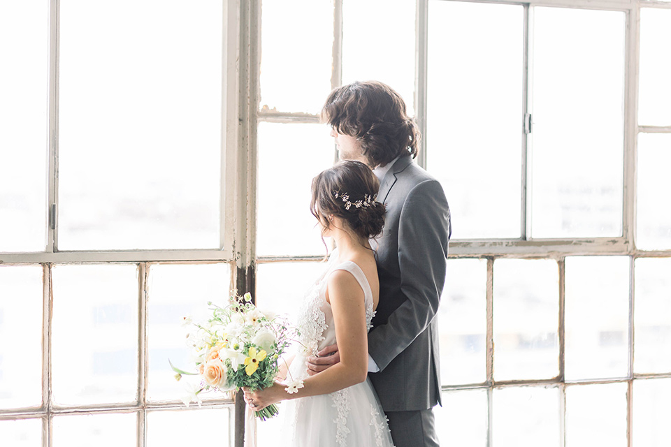 Spring-styled-shoot-bride-and-groom-looking-out-windows-the-bride-wearing-a-soft-tulle-gown-with-a-lace-sweetheart-neckline-and-a-soft-tulle-skirt-the-groom-in-a-grey-suit-with-a-deep-green-velvet-bow-tie