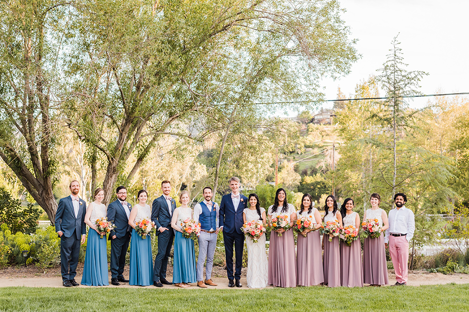 Supriya-and-Chris-wedding-bridal-party-for-traditional-ceremony-the-bridesmaids-in-two-toned-dresses-in-pink-and-blue-the-groomsmen-in-navy-suits-and-the-bride-in-a-white-lace-formfitting-gown-and-the-groom-in-a-navy-suit-with-pink-bow-tie