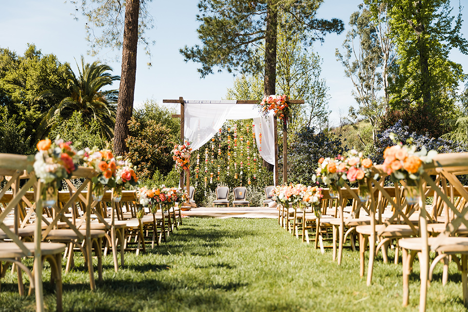 Supriya-and-Chris-wedding-ceremony-set-up-with-wooden-chairs-and-orange-and-yellow-flowers