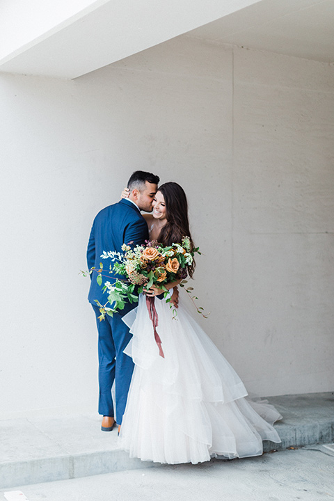 bride in a full tulle ballgown with a crystal and lace bodice and straps, groom in a blue suit with a floral tie and brown shoes