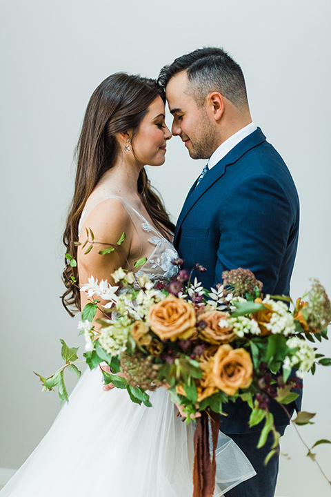 bride in a full tulle ballgown with a crystal and lace bodice and straps, groom in a blue suit with a floral tie and brown shoes