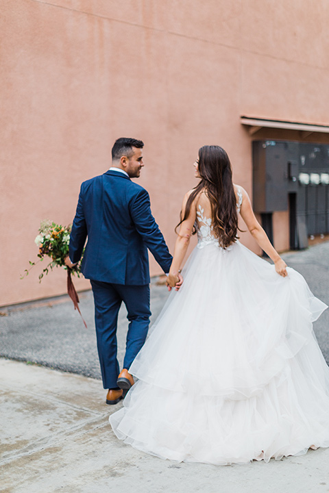 bride in a full tulle ballgown with a crystal and lace bodice and straps, groom in a blue suit with a floral tie and brown shoes