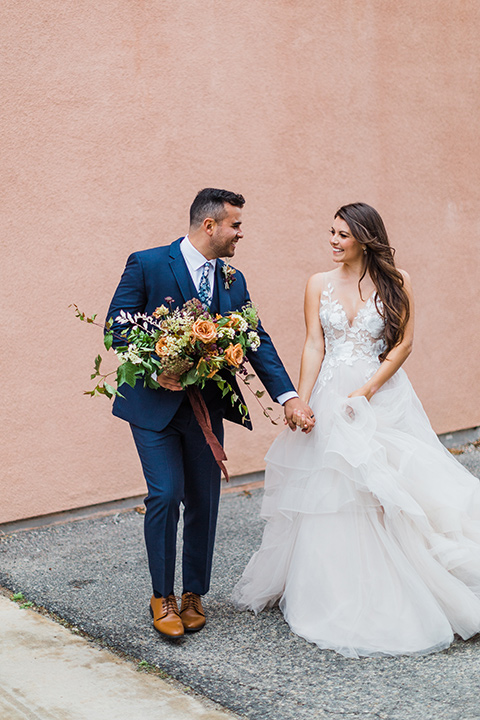  bride in a full tulle ballgown with a crystal and lace bodice and straps, groom in a blue suit with a floral tie and brown shoes 