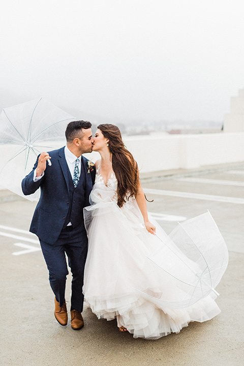  bride in a full tulle ballgown with a crystal and lace bodice and straps, groom in a blue suit with a floral tie and brown shoes 