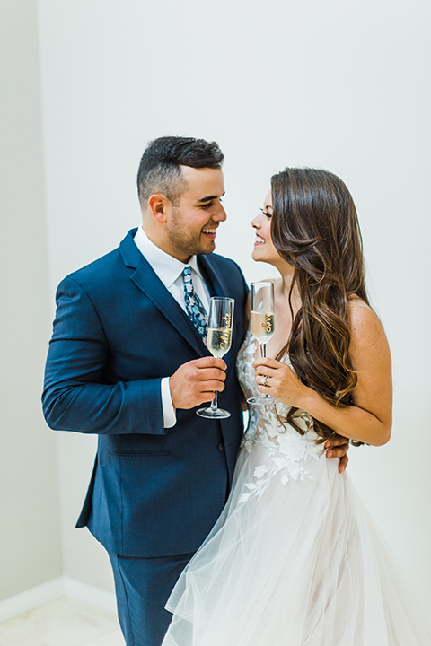  bride in a full tulle ballgown with a crystal and lace bodice and straps, groom in a blue suit with a floral tie and brown shoes 