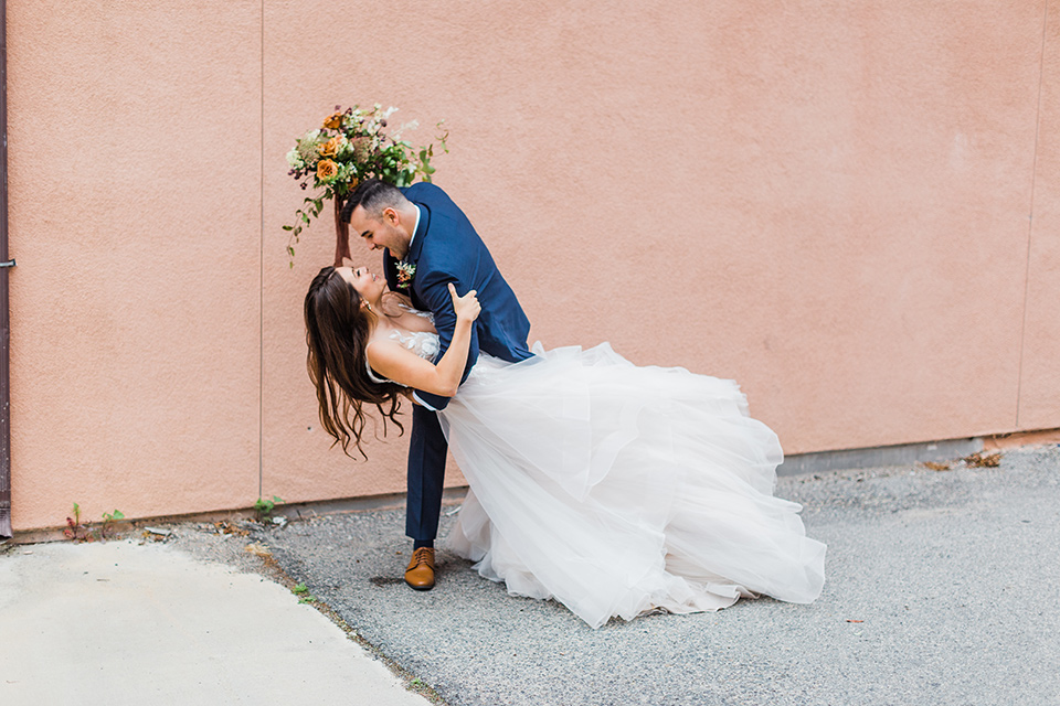 bride in a full tulle ballgown with a crystal and lace bodice and straps, groom in a blue suit with a floral tie and brown shoes