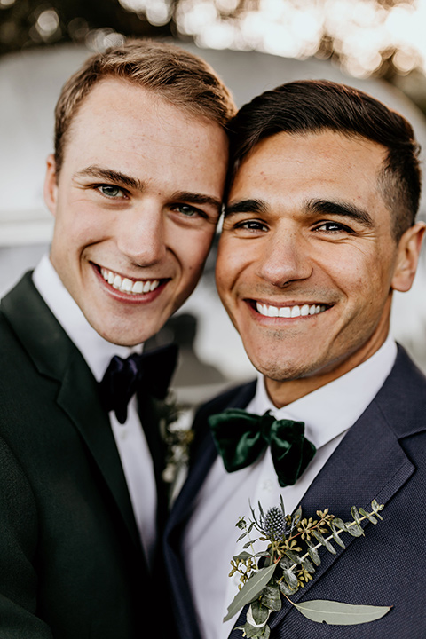 retro-ranch-styled-shoot-close-up-on-grooms-one-groom-wearing-a-dark-blue-suit-with-a-green-velvet-bow-tie-and-the-other-wearing-a-green-suit-with-a-blue-velvet-bow-tie