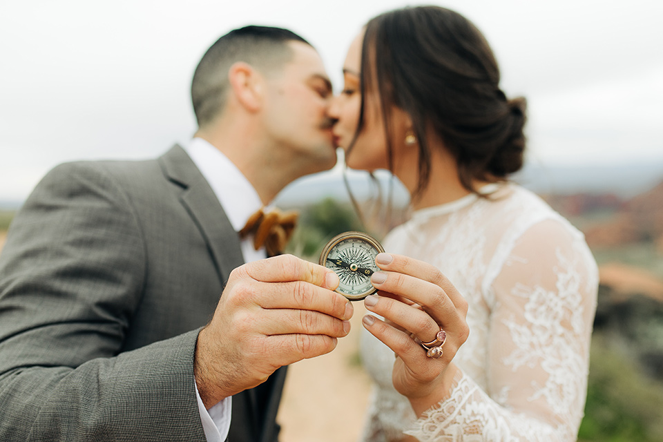 Utah-anow-canyon-shoot-bride-and-groom-holding-compass-the-bride-wears-an-olive-green-tulle-skirt-with-an-ivory-lace-long-sleeved-top-and-the-groom-in-a-café-brown-coat-with-a-dark-blue-pant-and-vest-with-a-gold-velvet-bow-tie