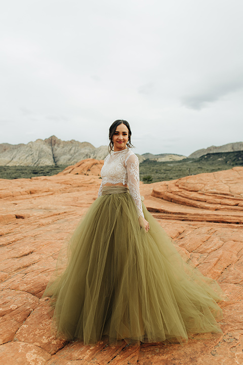 Utah-snow-canyon-shoot-bride-looking-over-her-shoulder-wearing-an-olive-green-tulle-skirt-and-an-ivory-lace-crop-top-with-long-sleeves