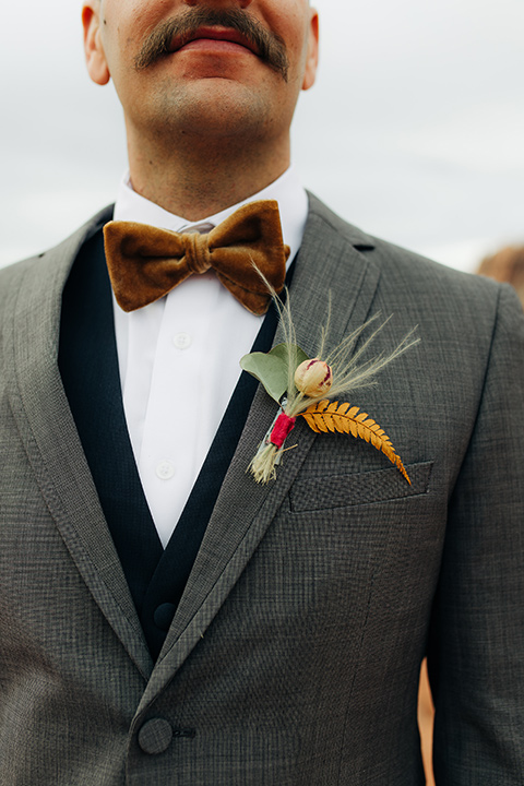 Utah-snow-canyon-shoot-groom-attire-close-up-in-a-café-brown-suit-with-blue-navy-pants-and-vest-with-a-gold-velvet-bow-tie