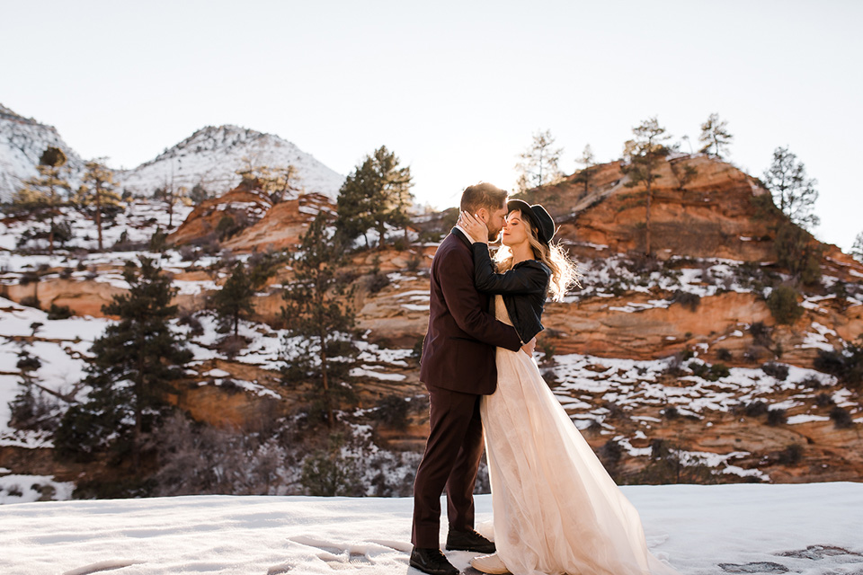 Utah-Shoot-bride-and-groom-kissing-bride-in-a-flowing-tulle-gown-and-lace-bodice-with-a-leather-jacket-while-the-groom-is-in-a-burgundy-tuxedo-with-a-long-black-tie