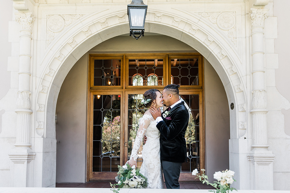 Maxwell-House-bride-and-groom-almost-in-front-of-the-venue-while-the-bride-is-wearing-a-lace-long-sleeved-gown-groom-in-a-black-velvet-tuxedo