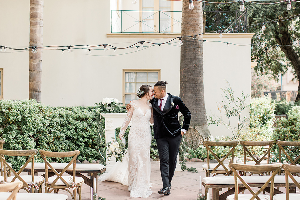 Maxwell-House-bride-and-groom-walking-away-from-ceremony-bride-is-wearing-a-lace-long-sleeved-gown-groom-in-a-black-velvet-tuxedo