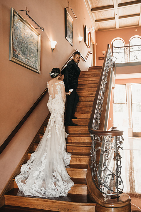 Maxwell-House-bride-and-groom-walking-up-the-stairs-bride-wearing-a-lace-long-sleeved-gown-groom-wearing-a-black-velvet-jacket