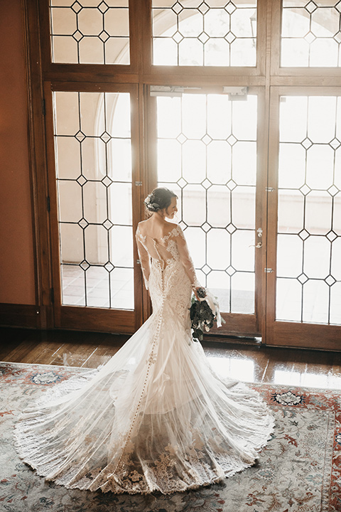 Maxwell-House-bride-by-the-windows-wearing-a-lace-gown-with-sleeves-with-a-deep-v-neckline