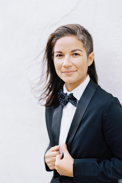 flower-market-shoot-bride-in-tux-looking-at-camera-bride-in-a-womens-black-shawl-lapel-tuxedo-with-polka-dot-bow-tie