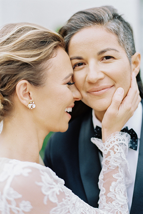 flower-market-shoot-close-up-on-couple-bride-in-a-womens-black-shawl-lapel-tuxedo-with-polka-dot-bow-tie-bride-in-tulle-ballgown-with-lace-sleeves