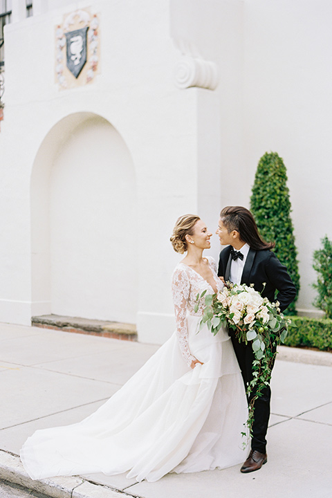 flower-market-shoot-bride-in-tux-looking-at-camera-bride-in-a-womens-black-shawl-lapel-tuxedo-with-polka-dot-bow-tie-bride-in-tulle-ball-gown-with-sleeves