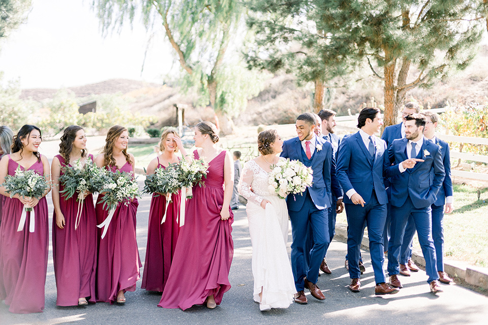 community-church-wedding-bridal-party-walking-bridesmaids-in-a-pink-berry-color-groomsmen-in-cobalt-suits-with-blue-ties-bride-in-a-flowing-gown-with-long-sleeves-and-an-illusion-bodice-groom-in-a-cobalt-blue-suit-with-a-berry-colored-tie