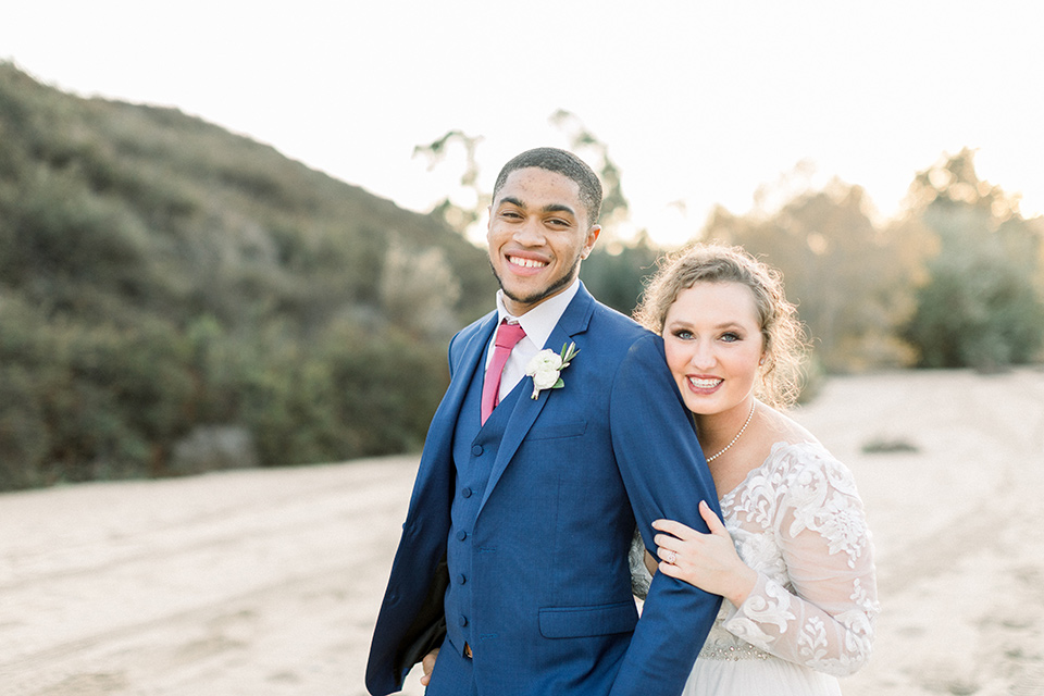 community-church-wedding-bride-and-groom-smiling-on-camera-bride-in-a-flowing-gown-with-long-sleeves-and-an-illusion-bodice-groom-in-a-cobalt-blue-suit-with-a-berry-colored-tie