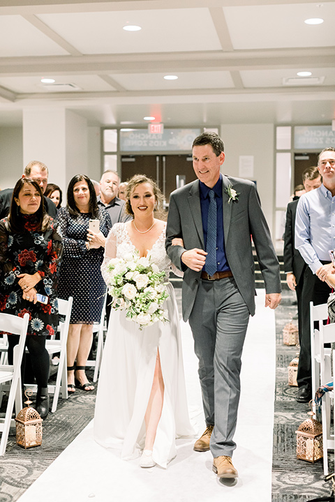 community-church-wedding-bride-walking-down-aisle-bride-in-a-flowing-gown-with-long-sleeves-and-an-illusion-bodice-groom-in-a-cobalt-blue-suit-with-a-berry-colored-tie