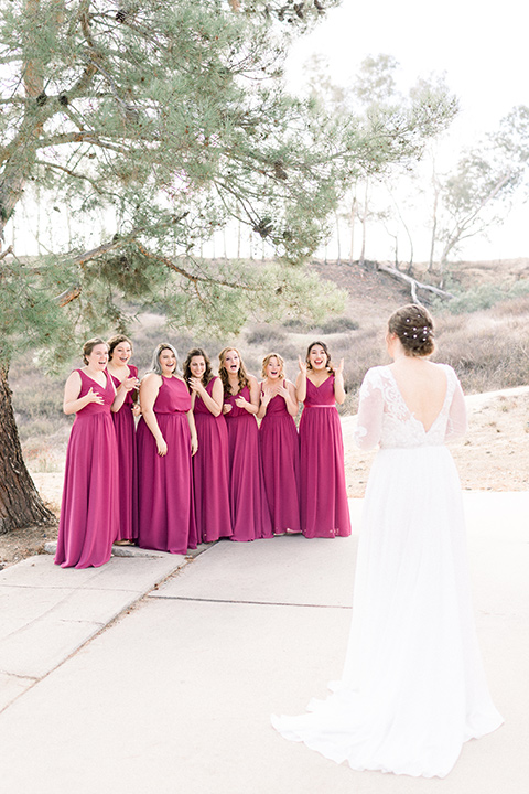 community-church-wedding-bridesmaids-seeing-bride-for-the-first-time-bride-in-a-flowing-boho-style-dress-with-sleeves-bridesmaids-in-berry-colored-dresses