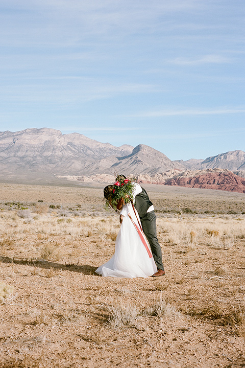 red-rocks-shoot-couple-kissing-behind0flowers-bride-in-a-flowing-white-gown-groom-in-a-grey-suit