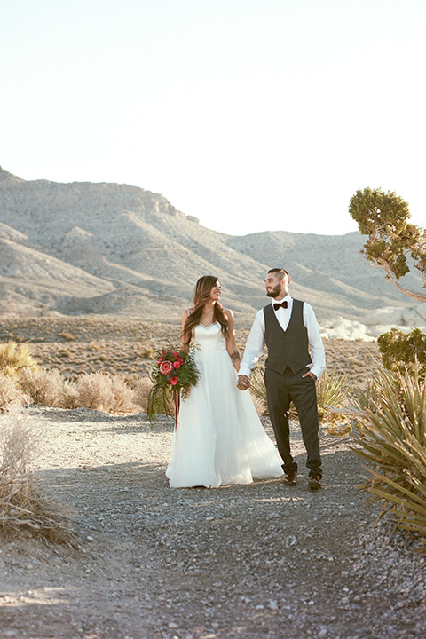 red-rocks-shoot-couple-walking-bride-in-a-flowing-white-gown-groom-in-a-grey-suit