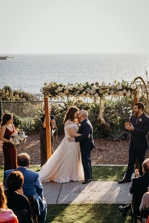 la-jolla-wedding-bride-and-groom-first-kiss-bride-in-a-tulle-ballgown-with-a-crystaled-bodice-and-cap-sleeves-groom-in-a-navy-suit-and-light-blue-shirt