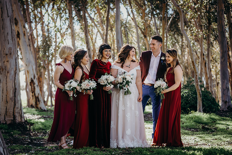 la-jolla-wedding-bride-and-her-bridesmaids-and-bridesman-bride-in-a-flowing-ball-gown-with-a-detailed-bodice-and-straps-bridesmaids-in-dark-burgundy-red-dresses