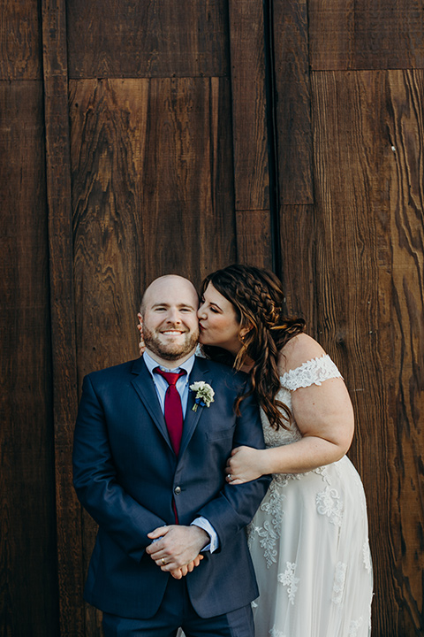 la-jolla-wedding-bride-kissing-groom-on-cheek-groom-in-a-dark-blue-suit-with-a-light-blue-shirt-and-red-tie-bride-in-a-tulle-ball-gown