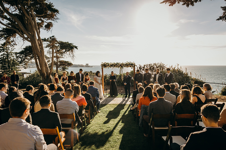 la-jolla-wedding-ceremony-bride-in-a-flowing-ball-gown-with-a-detailed-bodice-and-straps-groom-in-a-dark-blue-suit-with-a-light-blue-suit-and-red-tie