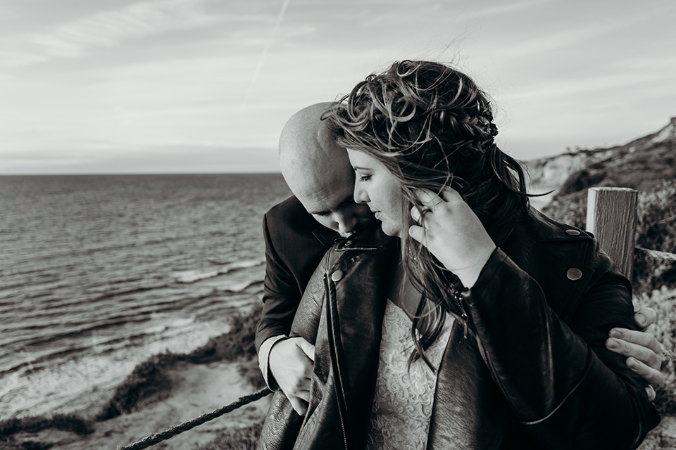 la-jolla-wedding-groom-kissing-bride-on-shoulder-bride-in-leather-jacket-bride-in-a-flowing-ball-gown-with-a-detailed-bodice-and-straps-groom-in-a-dark-blue-suit-with-a-light-blue-suit-and-red-tie