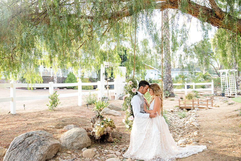 Blossom-valley-victorian-wedding-shoot-bride-and-groom-on-the-swing-bride-weaing-a-flowing-gown-with-straps-and-groom-wore-a-mix-and-match-look-with-a-dark-grey-coat-and-light-grey-pants