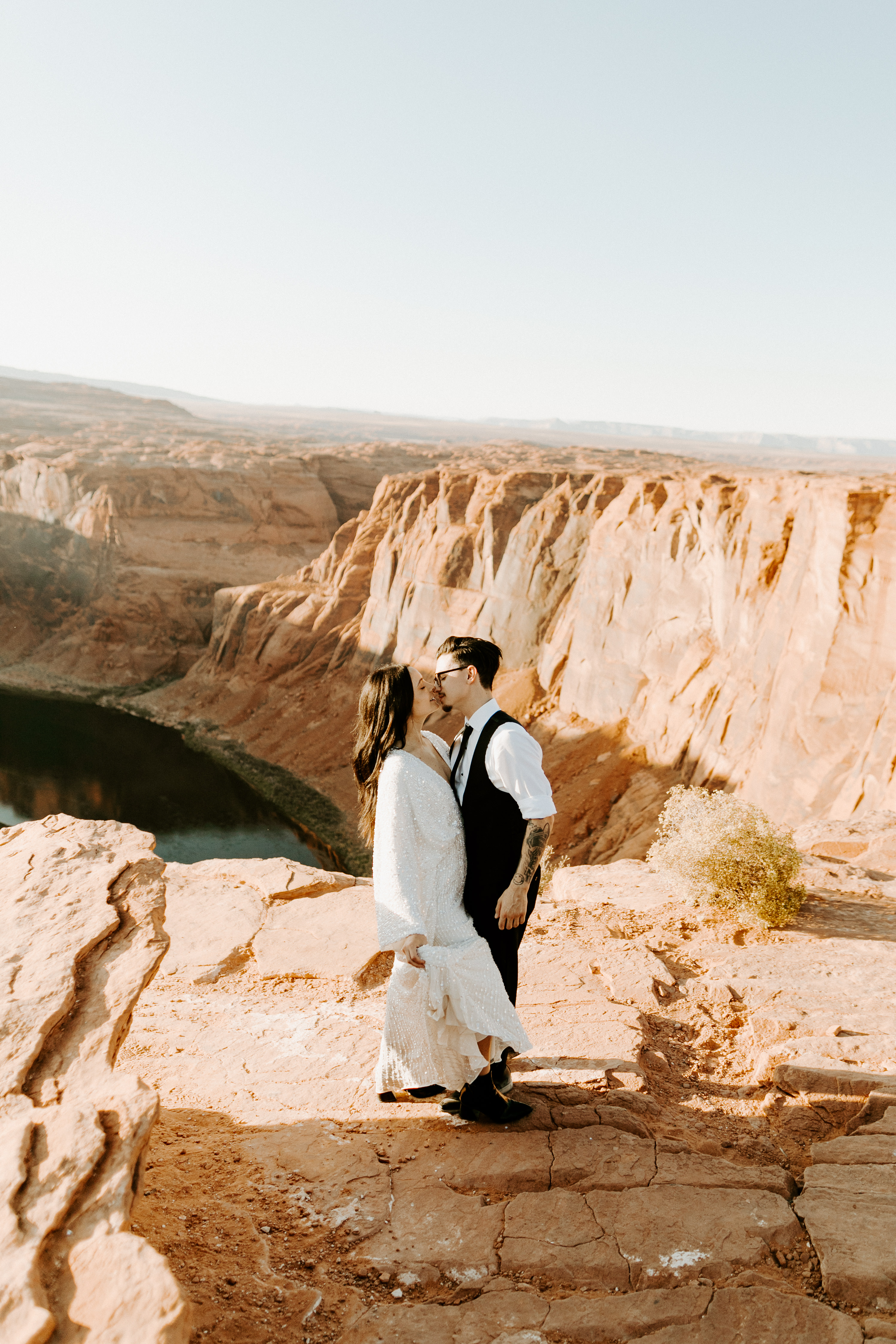  bride in an ivory long gown with bellowing sleeves and a boho design, groom in a black double-breasted vest and a white buttoned up shirt