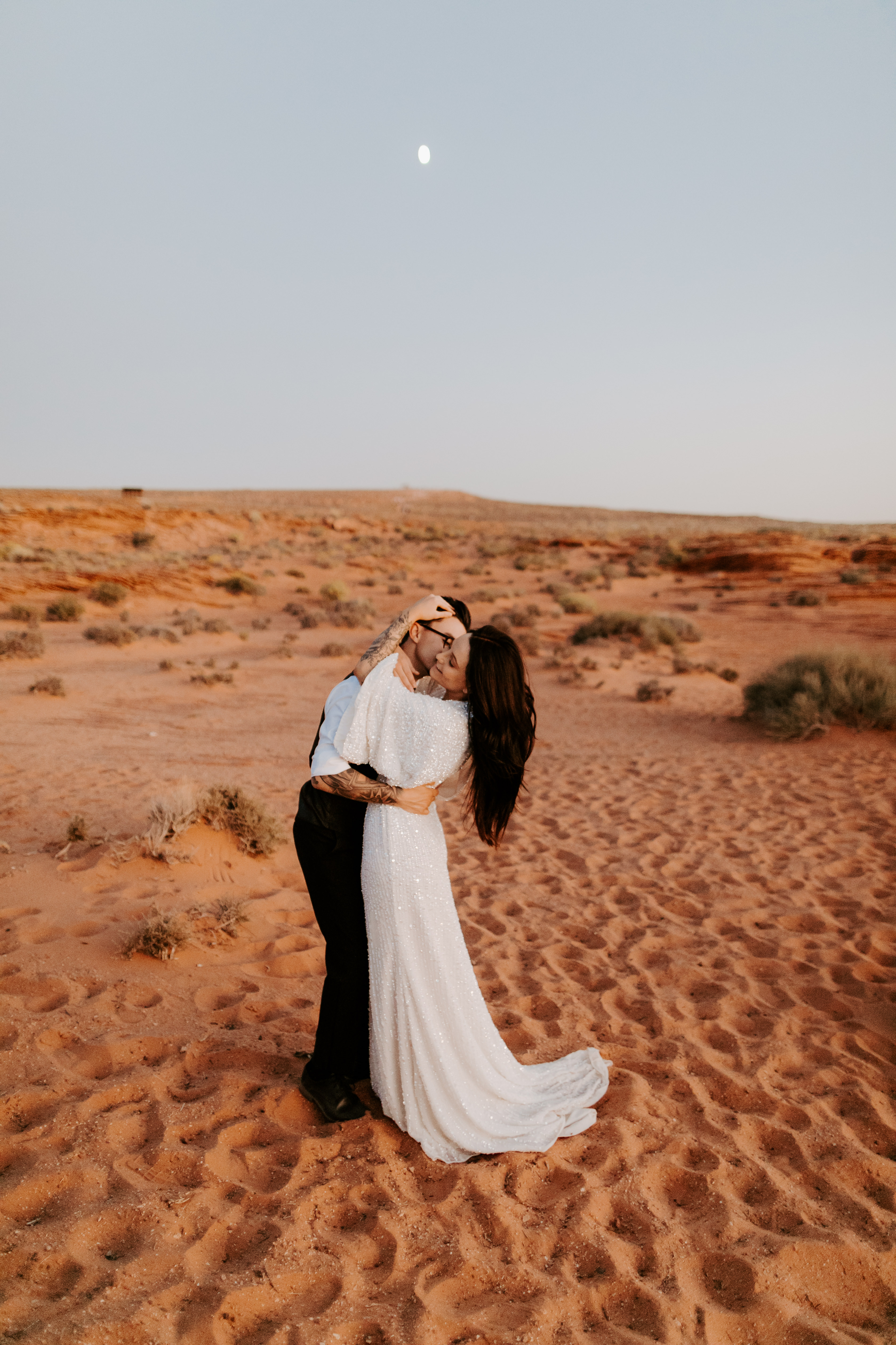  bride in an ivory long gown with bellowing sleeves and a boho design, groom in a black double-breasted vest and a white buttoned up shirt