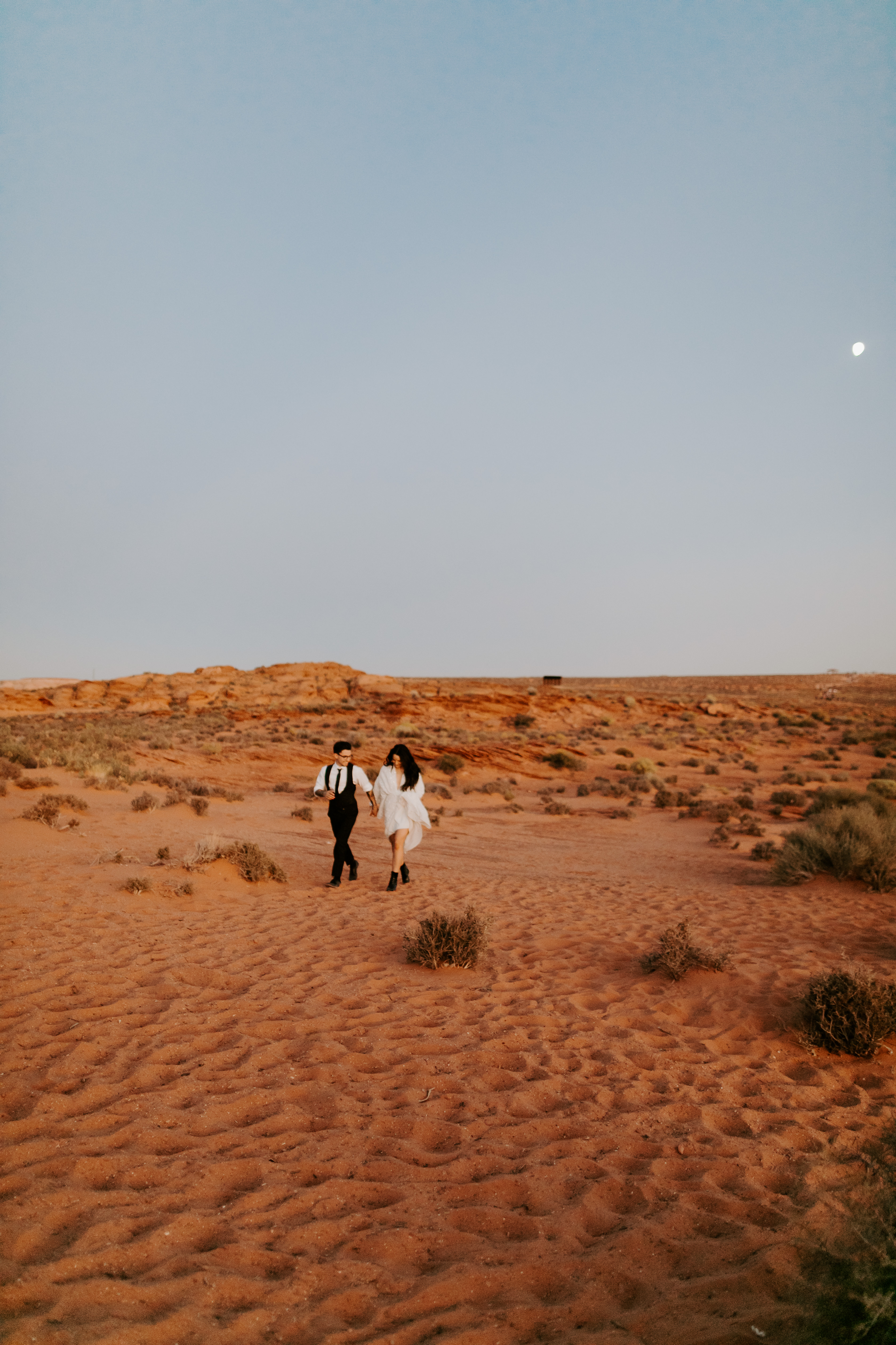  bride in an ivory long gown with bellowing sleeves and a boho design, groom in a black double-breasted vest and a white buttoned up shirt