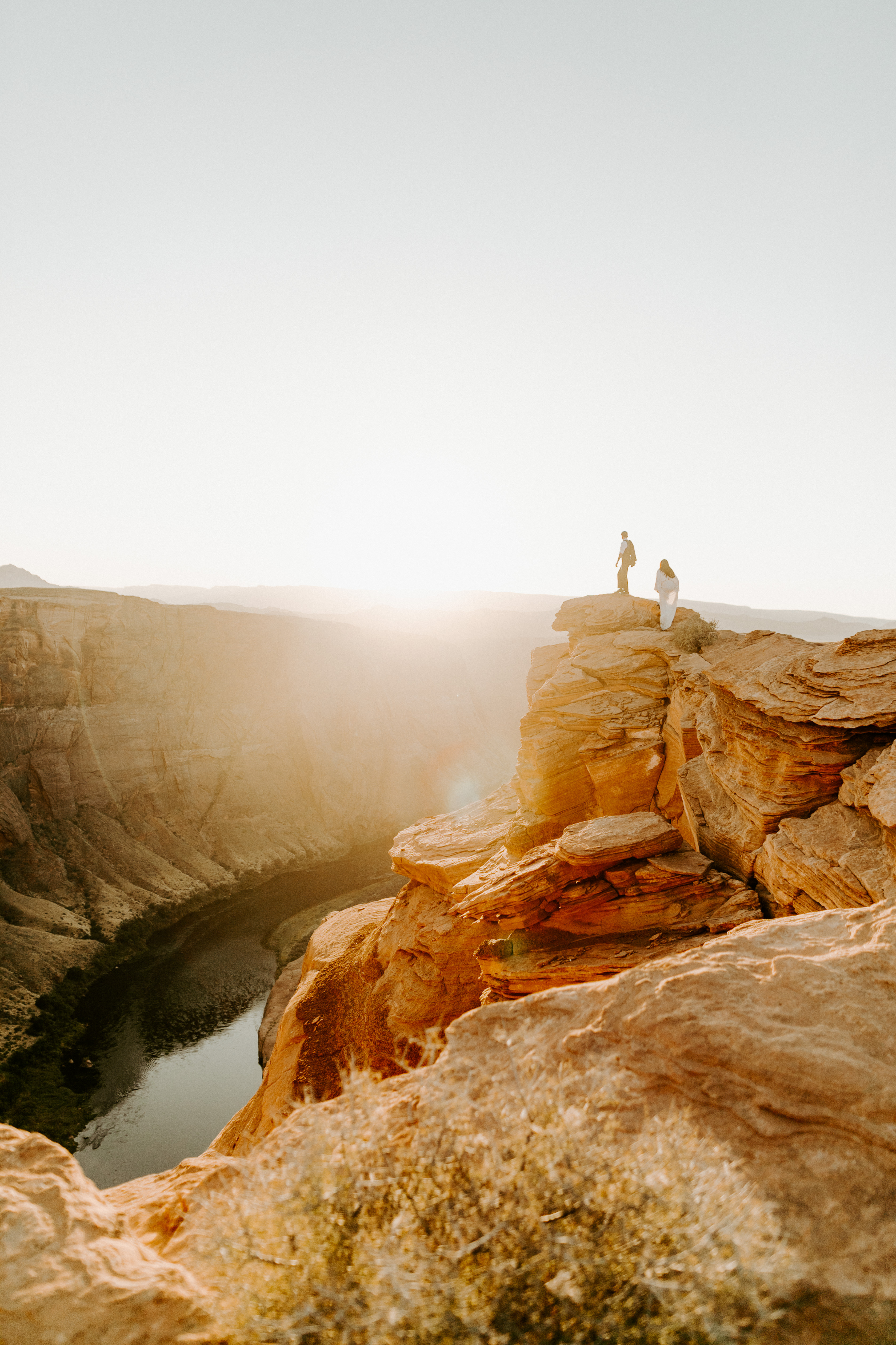  bride in an ivory long gown with bellowing sleeves and a boho design, groom in a black double-breasted vest and a white buttoned up shirt on horseshoe bend