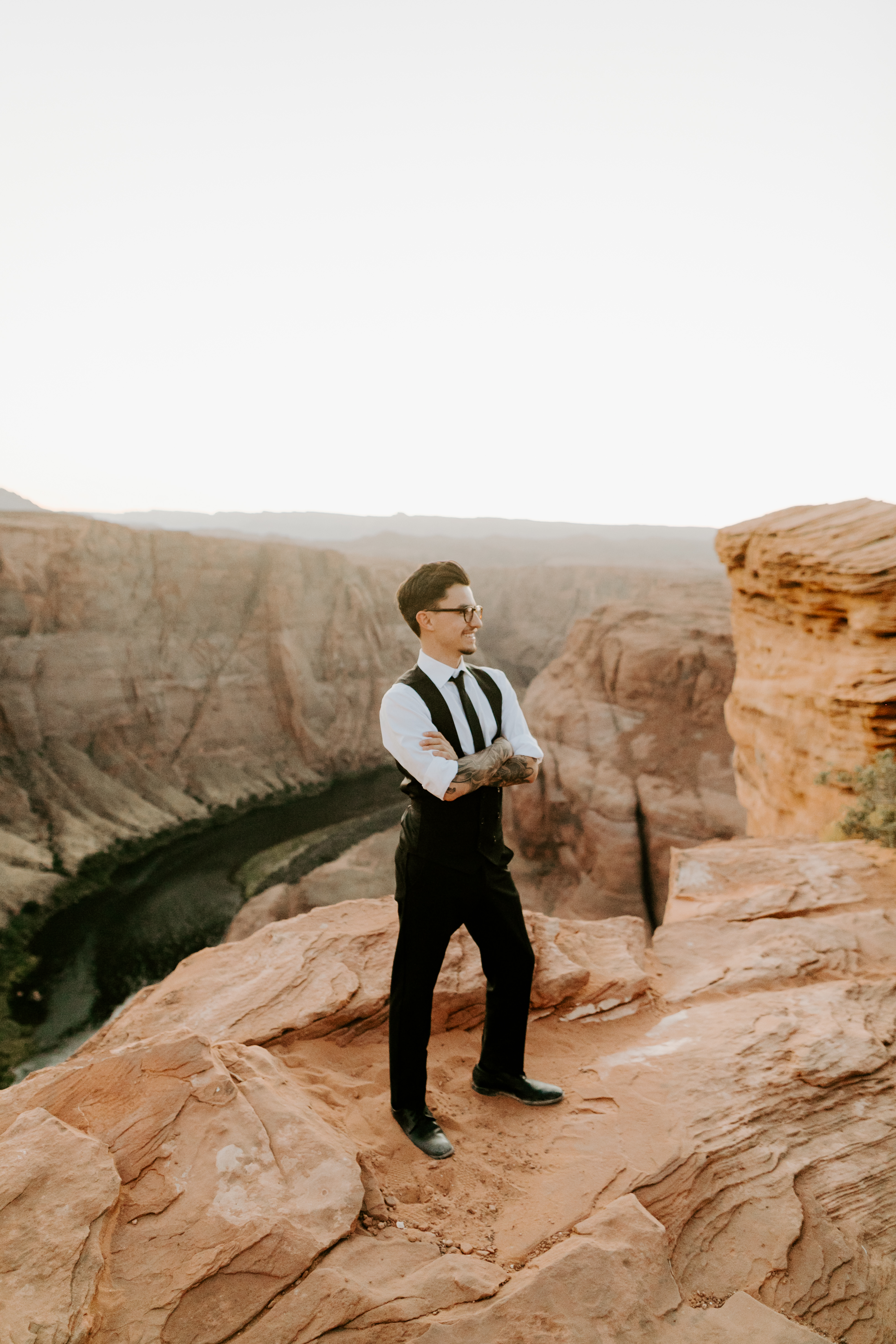  groom in a black double-breasted vest and a white buttoned up shirt sitting on cliffside